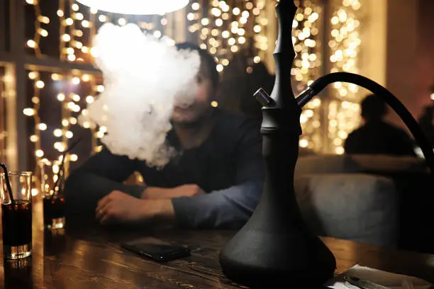 Photo of man holding hookah pipe and smoking in a night club