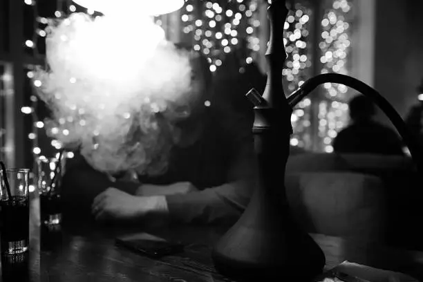Photo of man holding hookah pipe and smoking in a night club