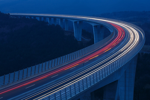 Blurred lights of vehicles driving on a tall viaduct with wind barriers, long exposure. Rush hour, on the road, connectivity and internet concept, background with copy space.