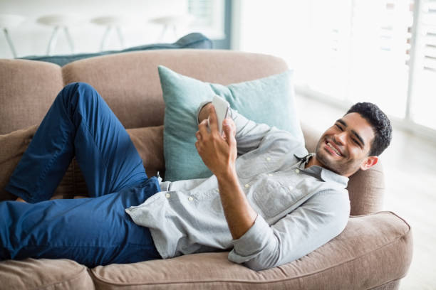 istock Man lying on sofa and using mobile phone in living room at home 656159548