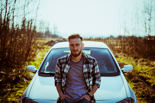 Young handsome man leaning on car his at countryside.