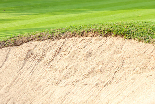 Close-up border of sand bunker contrasting on fresh grass in green golf course.