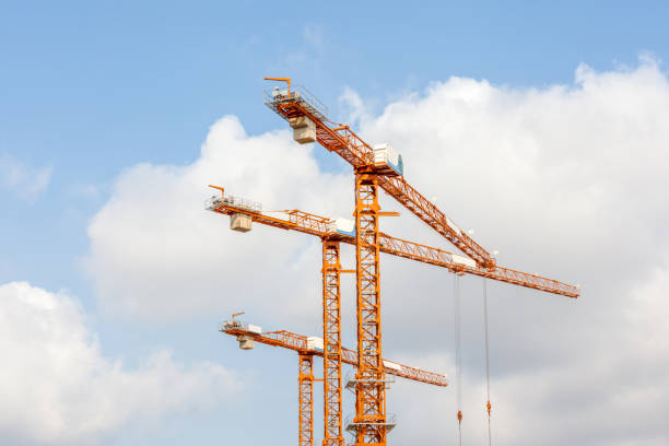 Three hoisting cranes with pulley and hook in construction site against blue sky background.