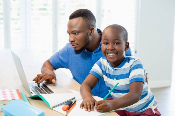 istock Father using laptop and son doing his homework in living room 656207878