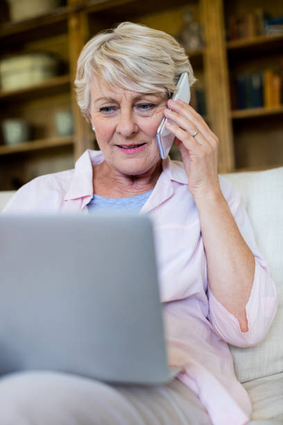 istock Senior woman talking on mobile phone while using laptop in living room 656213840