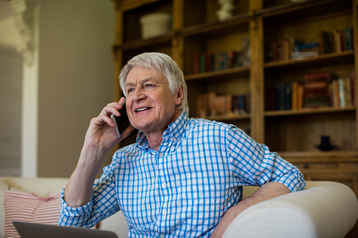 Senior man talking on mobile phone in living room at home