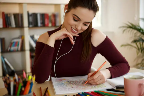 Beautiful young woman coloring book and listening music on headphones