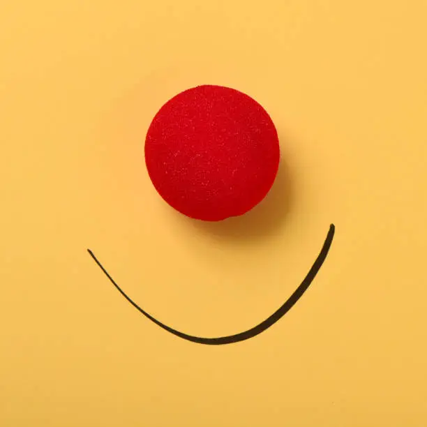 a red clown nose and a smile drawn on a yellow background