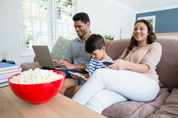 Mother watching television while father and son using laptop and digital tablet Mother watching television while father and son using laptop and digital tablet at home popcorn snack bowl isolated stock pictures, royalty-free photos & images