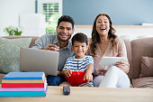 Son watching television while father and mother using laptop and digital tablet at home