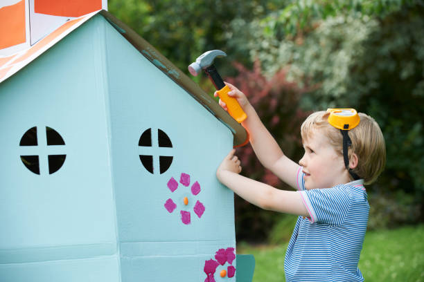 Young Boy Pretending To Fix Cardboard Playhouse Young Boy Pretending To Fix Cardboard Playhouse cardboard house stock pictures, royalty-free photos & images