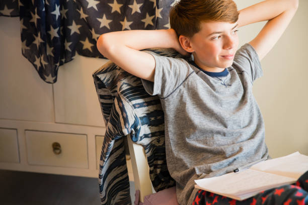 頭の後ろで手で宿題をしている自信のある少年 - kid reading ストックフォトと画像