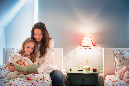 Mother and daughter reading book in bedroom