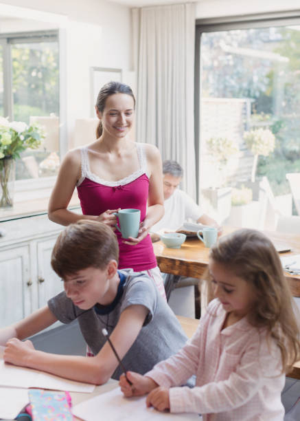 istock Mother with coffee watching daughter and son doing homework 656287183