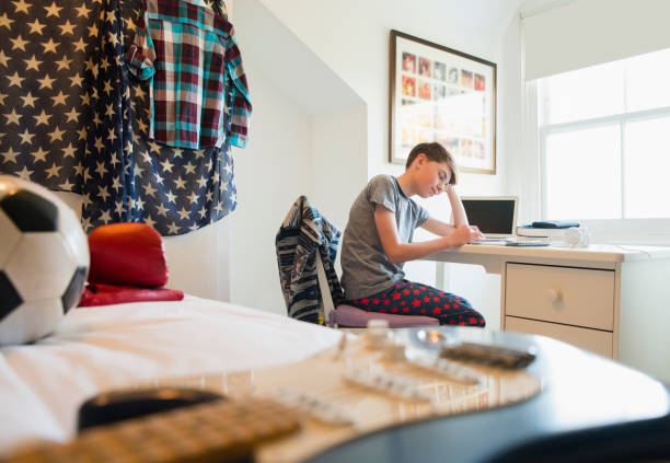 寝室の机で宿題をしている退屈な少年 - kid reading ストックフォトと画像