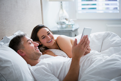 Smiling couple laying in bed using digital tablet