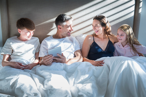 Smiling family laying in bed using digital tablet
