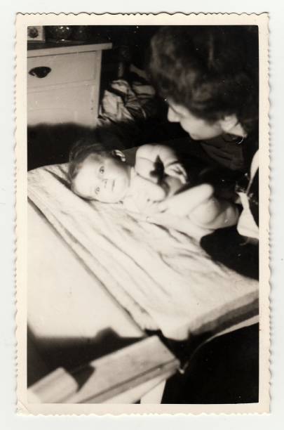 Hodonin,Czechoslovak Republic - August 26, 1940: Vintage photo shows a small baby girl with her aunt. Photography shows old white kitchen. Cupboard on background.
