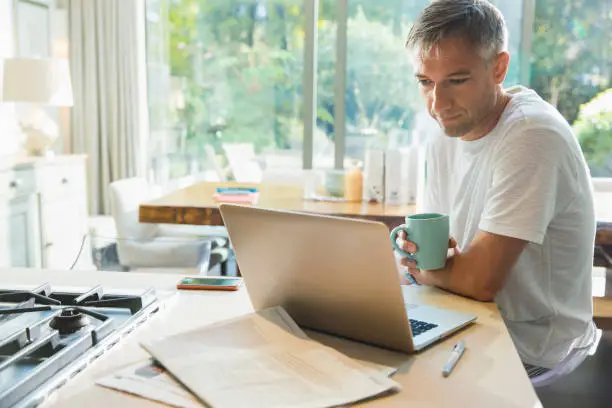 Photo of Man drinking coffee and working at laptop in kitchen