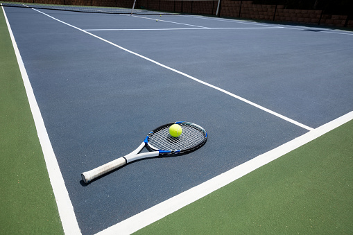 Tennis racquet and ball in court on a sunny day