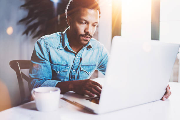 istock Pensive bearded African working at home while sitting the wooden table.Using modern laptop for new job search.Concept of young people work mobile devices.Blurred background,flare effect. 656324332
