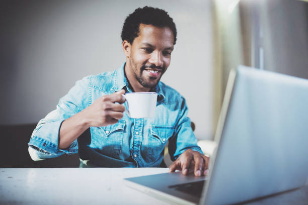 istock Smiling young African man making video conversation via laptop with partners while drinking white cup black tea in meeting office.Concept of happy business people.Blurred background,film effect. 656324476