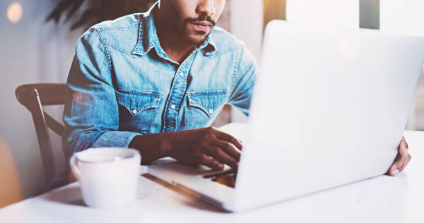 istock Pensive bearded African working at home while sitting the wooden table.Using modern laptop for new job search.Concept of young people work mobile devices.Blurred background,flare effect,crop. 656325898
