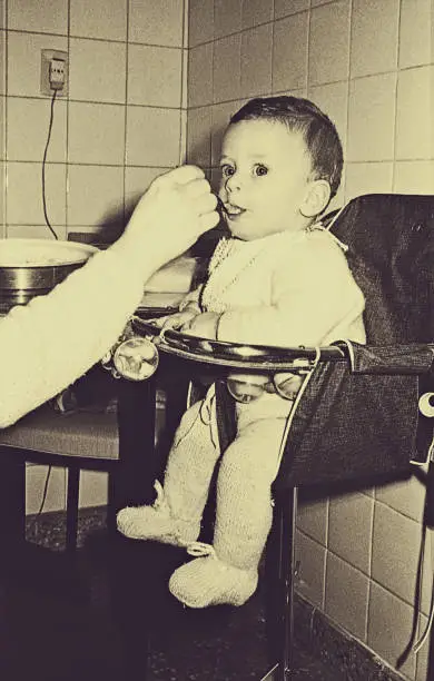 Vintage photo of a baby from the sixties being fed in a vintage kitchen.