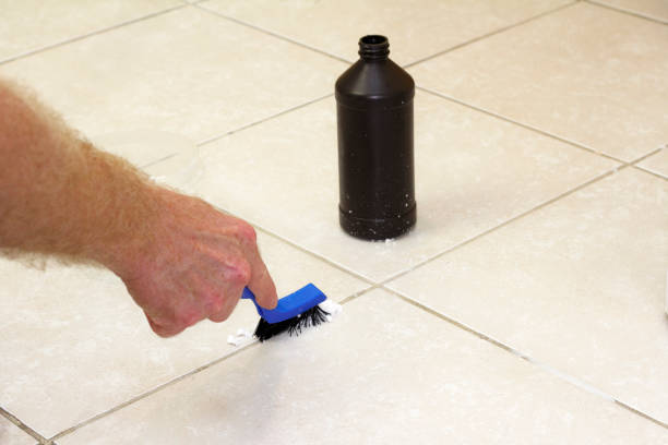 Cleaning Floor Grout with Baking Soda Hand with a blue handled black scrub brush cleaning grout with baking soda and peroxide. Floor grout tile being cleaned with baking soda and hydrogen peroxide. hydrogen peroxide stock pictures, royalty-free photos & images