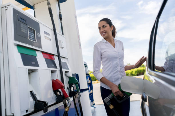 Woman refueling her car at a petrol station Happy woman refueling her car at a petrol station and holding the fuel pump - transportation concepts refueling stock pictures, royalty-free photos & images