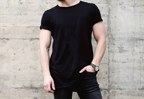 closeup view of young bearded man wearing black tshirt and jeans posing in center of modern city. empty concrete wall on the background. hotizontal mockup. - hotizontal imagens e fotografias de stock