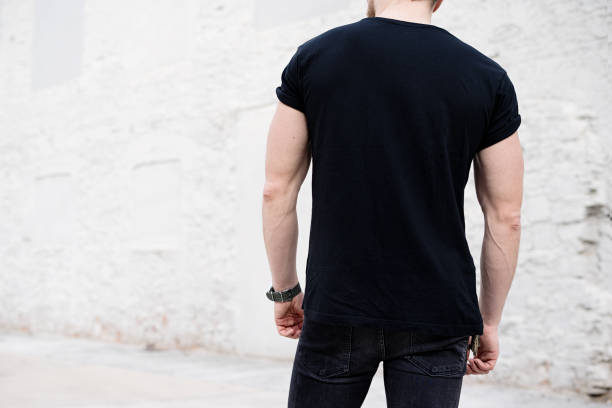 junge muskulöse bärtige mann mit schwarzen t-shirt und jeans posiert im zentrum der modernen stadt. leere betonwand auf dem hintergrund. hotizontal mockup, rückansicht - hotizontal stock-fotos und bilder