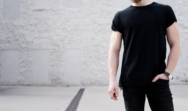 istock Young muscular bearded man wearing black tshirt and jeans posing outside. White bricks wall on the background. Hotizontal mockup, front view 656357674