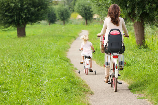 Rear view portrait of mother and daughter riding bicycles in park