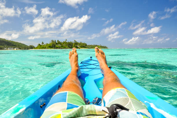 Stunning view of a young man's legs in a kayak near Motu Koromiri, a small island in the lagoon of Rarotonga near Muri Beach. Cook Islands in the South Pacific Ocean, Clear, shallow water, palm trees. stock photo