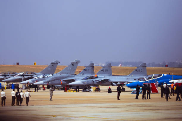 Airplanes lineed up bangalore, Karnataka, India - 02/16/2017 : Taken this picture at Aero India in Bangalore of the fighter planes lined up. In the line up are the French Rafales, Swedish Gripen and BAE Hawk which are participating in the air show. In the foreground are the spectators and people enjoying the show. british aerospace stock pictures, royalty-free photos & images
