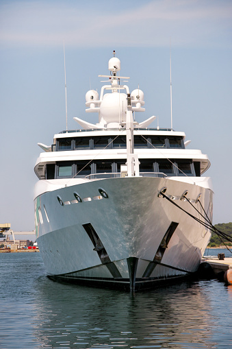 Bow of large modern luxury white yacht and ship anchored in harbor. Large white modern motorboat super yacht and ship in the port city of Pula, Croatia. Yachting concept.