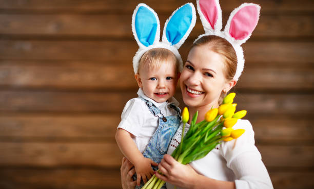 ¡feliz pascua de resurrección! madre y bebé en orejas de conejo con flores amarillas - vacations two generation family holiday easter fotografías e imágenes de stock