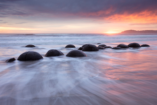 New Zealand. Just after high tide at sunrise, waves break around the Moeraki Boulders. These are large spherical boulders lying on the beach on the Otago coast about 75 km north of Dunedin. Each boulder can be up to 2 meters across.