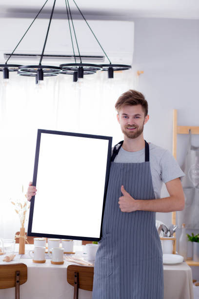 istock handsome chef showing blank empty board menu sign for restaurant menu or recipe with food table background. 656456498