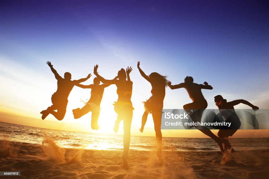 Gli amici felici saltano il tramonto sulla spiaggia. Amicizia o concetto di squadra - Foto stock royalty-free di Spiaggia