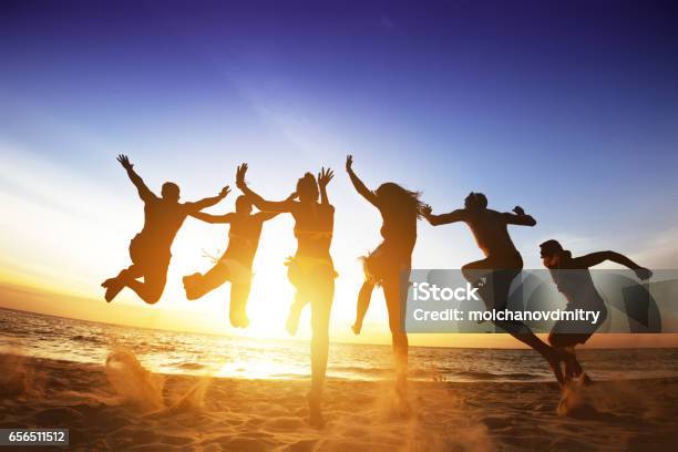 Gli Amici Felici Saltano Il Tramonto Sulla Spiaggia Amicizia O Concetto Di Squadra - Fotografie stock e altre immagini di Spiaggia