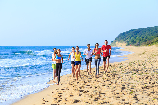 Team exercising on beach, running. All with sportswear. Sea and nature on background.