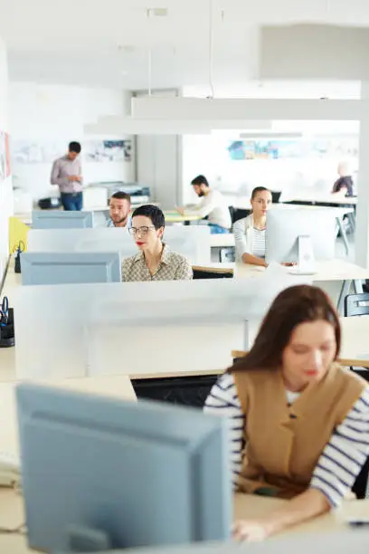 Separate workplace cubicles with different people sitting at them in open space of modern office