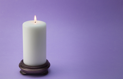 Single white lit candle on wood holder isolated on lilac / mauve background