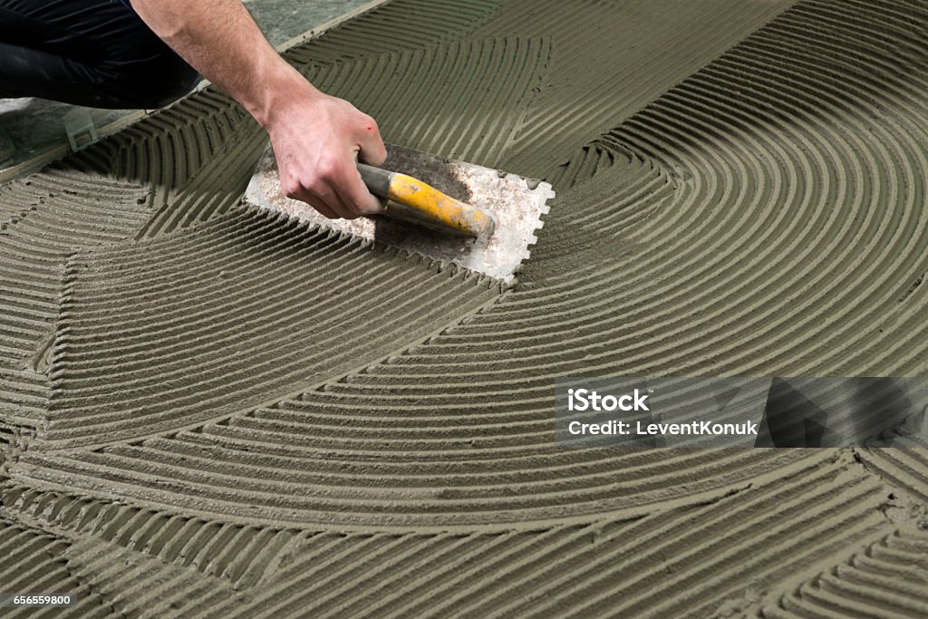 Construction Worker Applying Ceramic Glue Handyman applying cement adhesive for ceramic tile on floor. Cement Stock Photo