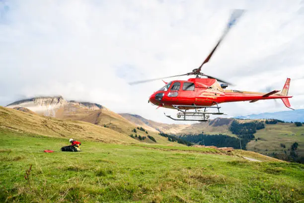 Mountain rescue helicopter takes off from green mountainside in the Swiss Alps. The helicopter is used for mountain rescue as well as general transportation in the mountainous Bernese Oberland region.