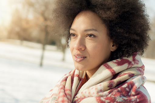 Portrait of beautiful young woman with Christmas blanket enjoying winter sunshine