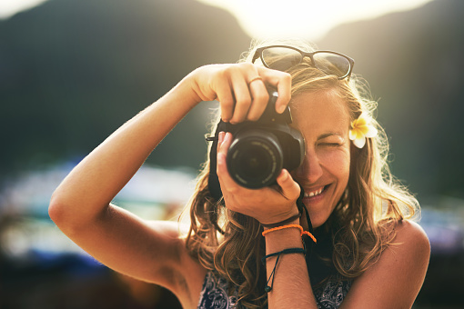 Portrait of a young woman taking photos with her camera at the beach