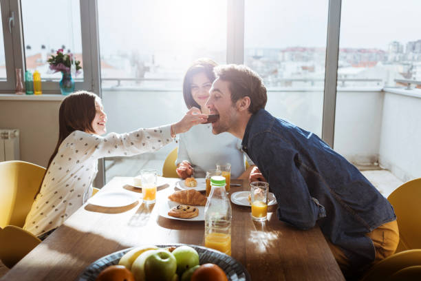 daughter feeding her dad at breakfast stock photo